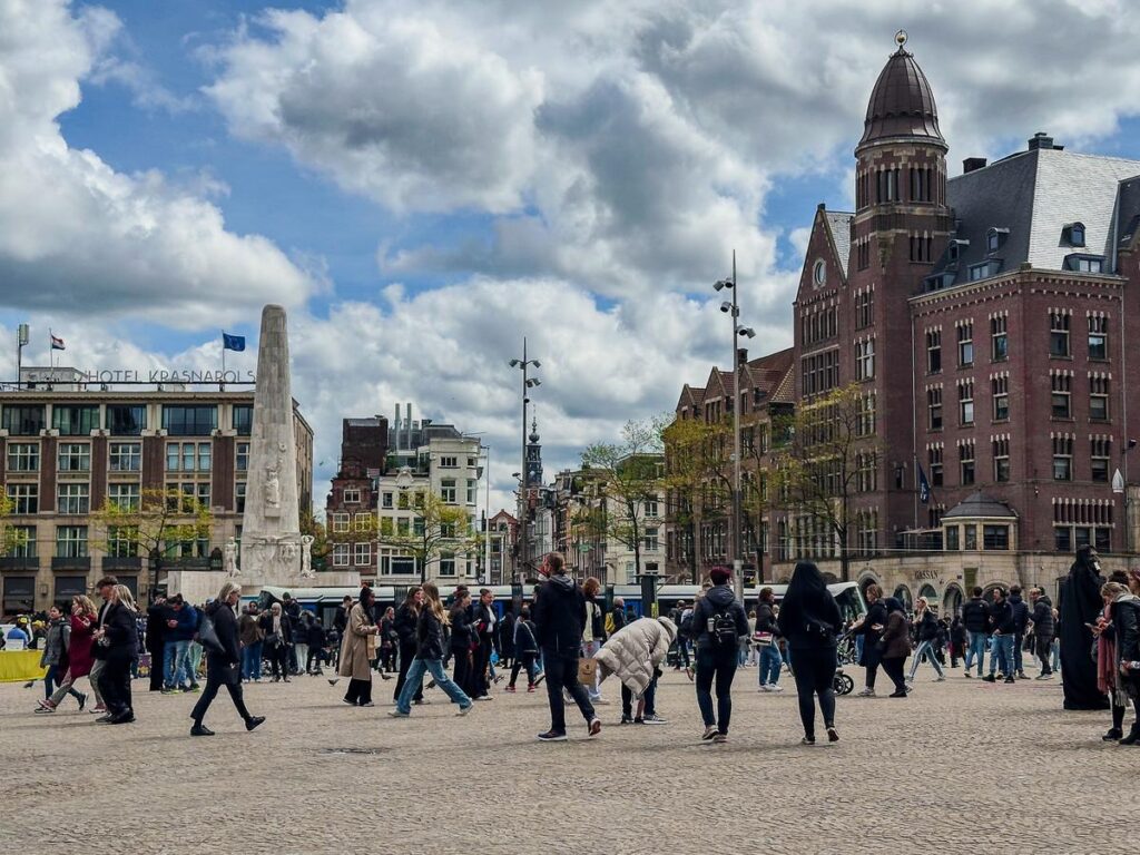 City life at Dam Square in Amsterdam under a dynamic sky, featuring pedestrians and historic architecture.
