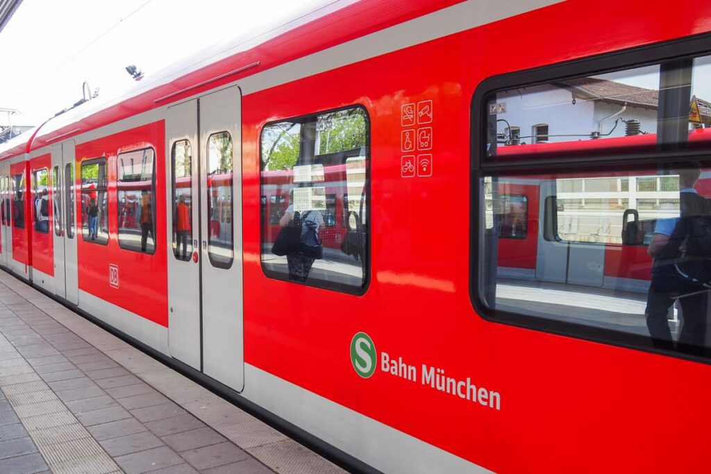 Red Munich S-Bahn train at platform, showcasing city transport with clear signage and accessible features, set against urban backdrop