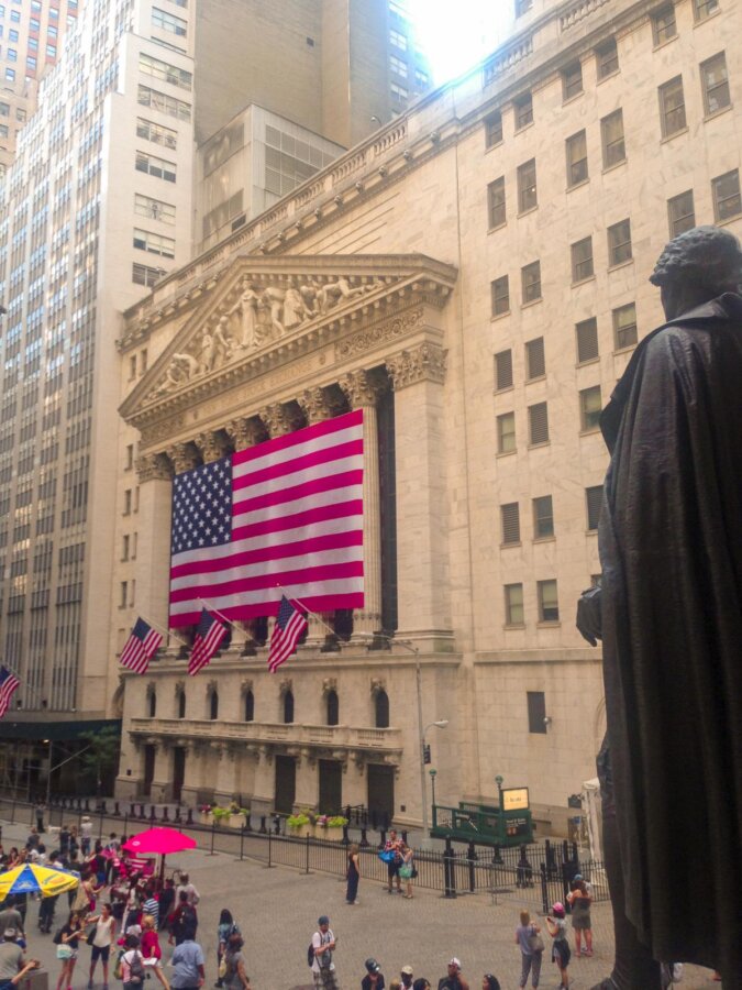 Busy NYSE on Wall Street with American flags and statue