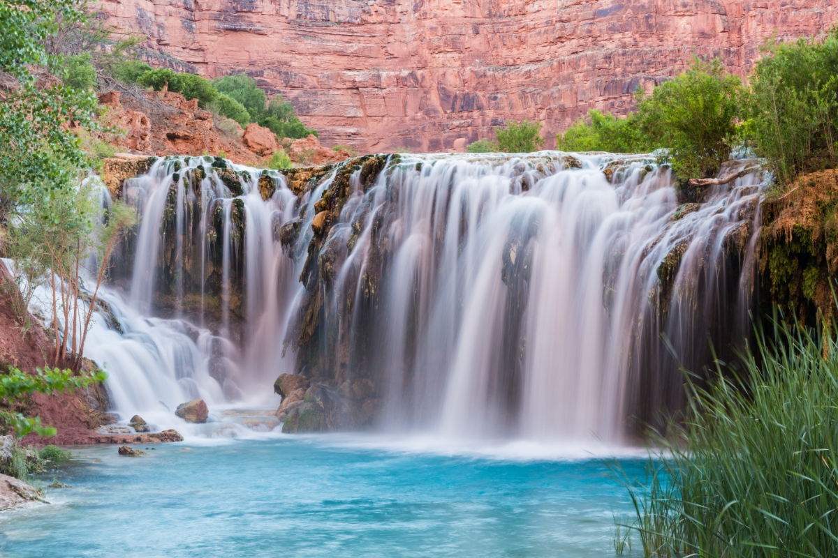 Navajo Falls, Havasupai Indian Reservation over red sandstone canyon into turquoise pool with lush vegetation, reeds and moss.