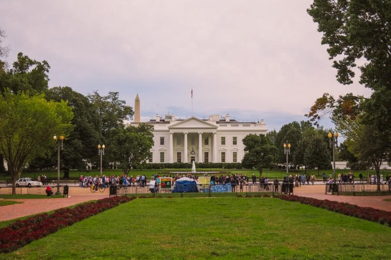 Tourists at the White House under a cloudy sky with view of the Washington Monument