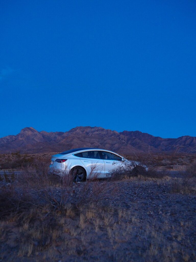 A white Tesla Model 3 set against a tranquil Mojave Desert landscape as the evening sky darkens.