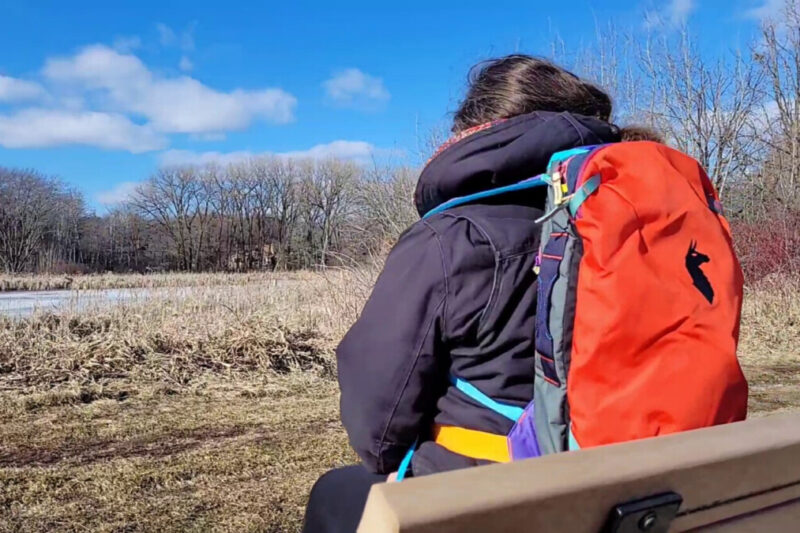 Woman on bench with colorful Cotopaxi backpack outdoors.