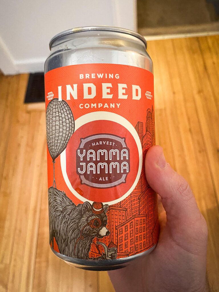 Hand holding Indeed Brewing's Yamma Jamma Ale can with bear and urban skyline art.