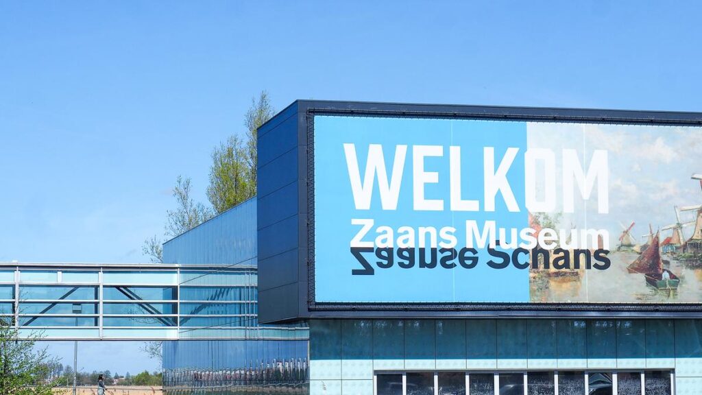 Exterior of Zaans Museum with WELKOM sign, traditional windmills, under sunny blue sky.