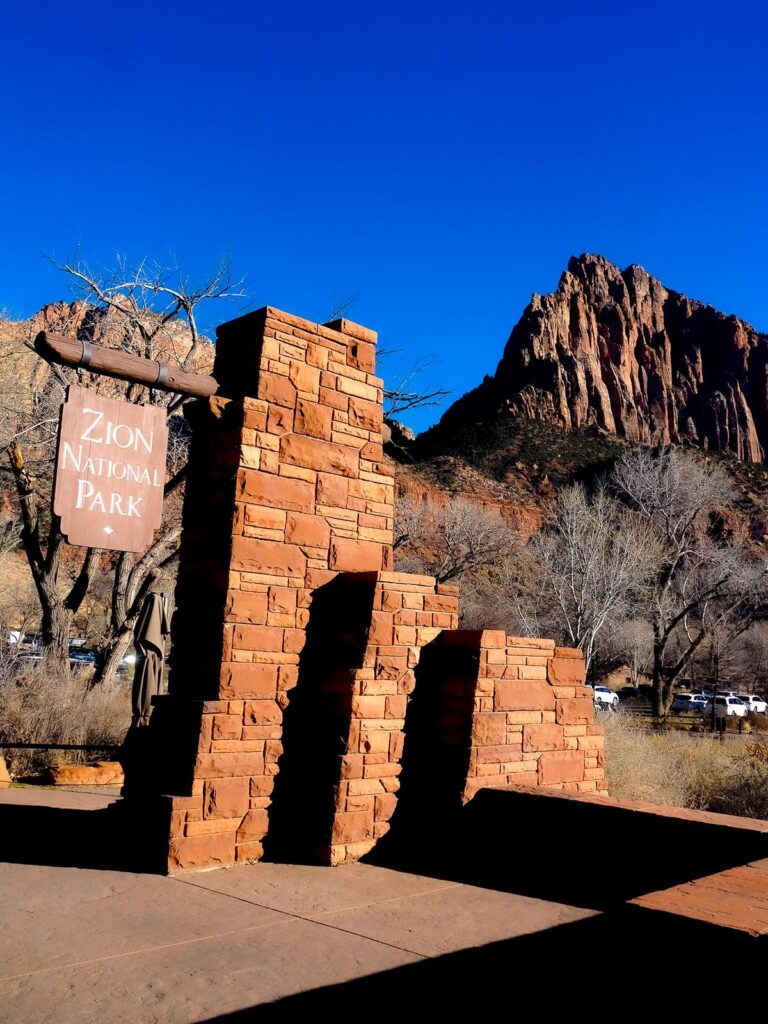 Zion National Park entrance sign with red sandstone archway and towering sandstone cliffs.